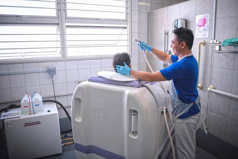 Right: Ren Ci Community Hospital nurse Maroger Paningbatan, 28, pushing a patient into the Viami RS-05 shower machine. The patient is seated on a specially designed commode chair. Below: While the machine washes the patient's body, the nurse can wash