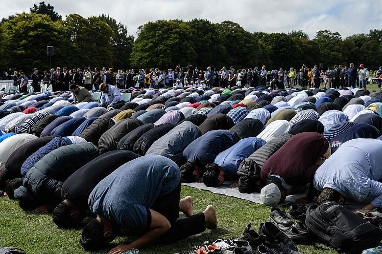 Above: Muslim men praying in a park near the Al Noor Mosque in Christchurch, shortly after two minutes of silence was observed yesterday in memory of the victims. Left: A police officer outside the Kilbirnie Mosque in Wellington. New Zealand has been