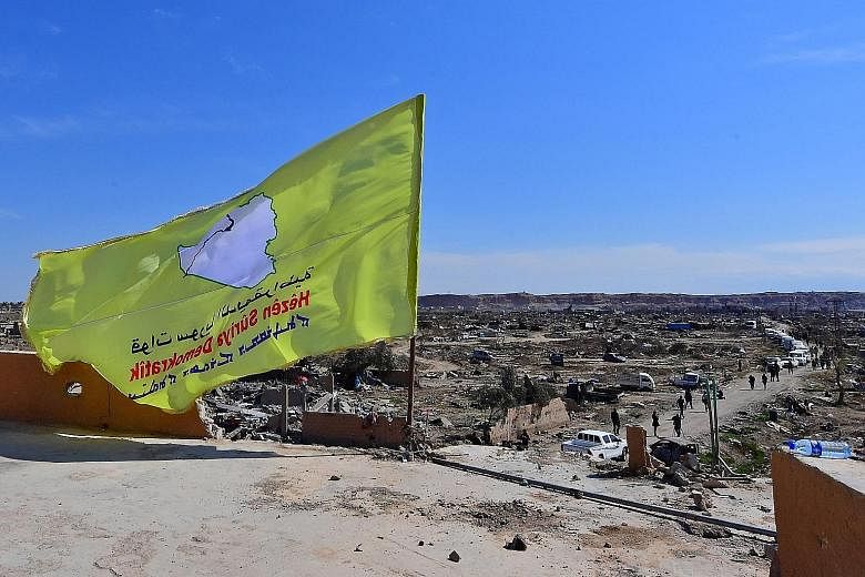 Left: The Syrian Democratic Forces hoisted their yellow flag atop a bullet-riddled building in the Syrian village of Baghuz yesterday, proclaiming the "total elimination" of ISIS' so-called caliphate. Below: Smoke rising over Baghuz, which was litter