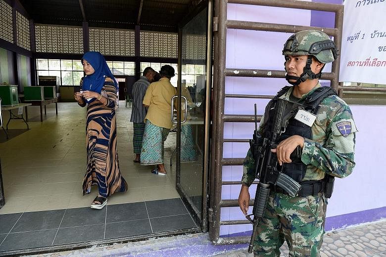Voters at a polling station in a local car service centre in the Huay Kwang district of Bangkok yesterday. Millions of Thais braved long queues and blistering heat to vote in the long-awaited elections. An election official presenting a ballot for in