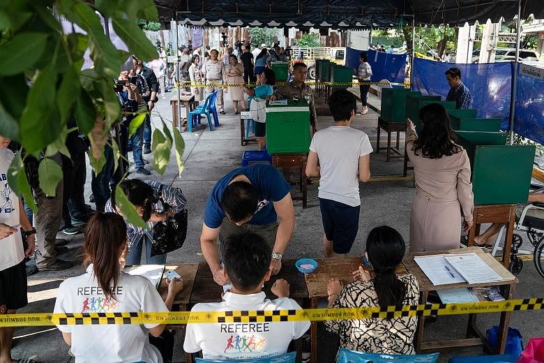 Left: Voters checking in at a polling station in Bangkok yesterday. Around 51 million Thais were eligible to vote, casting a single ballot for their preferred constituency candidates. Right: Voters casting their ballots in Bangkok's Thawiwit School y