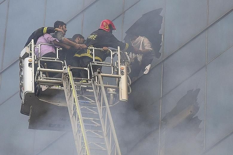 Firefighters rescuing a person from the burning office building in Bangladesh's capital city. A person trying to climb down Dhaka's FR Tower to escape a fire which broke out inside the building yesterday. A large crowd outside the 22-storey office bu