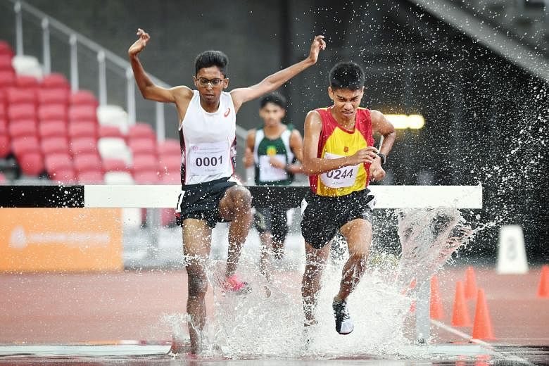 Ruben Loganathan (white top) and Joshua Rajendran locked in battle before the ASRJC runner surged ahead to win the A Div boys' 3,000m steeplechase in 10:24.85 at the National Stadium yesterday.