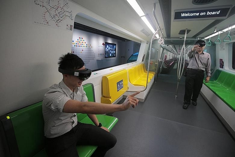 LTA project engineer Edmund Lee (left) and senior project engineer Liu Jiahan demonstrate using augmented reality glasses inside a replica MRT train cabin at the Singapore Mobility Gallery.