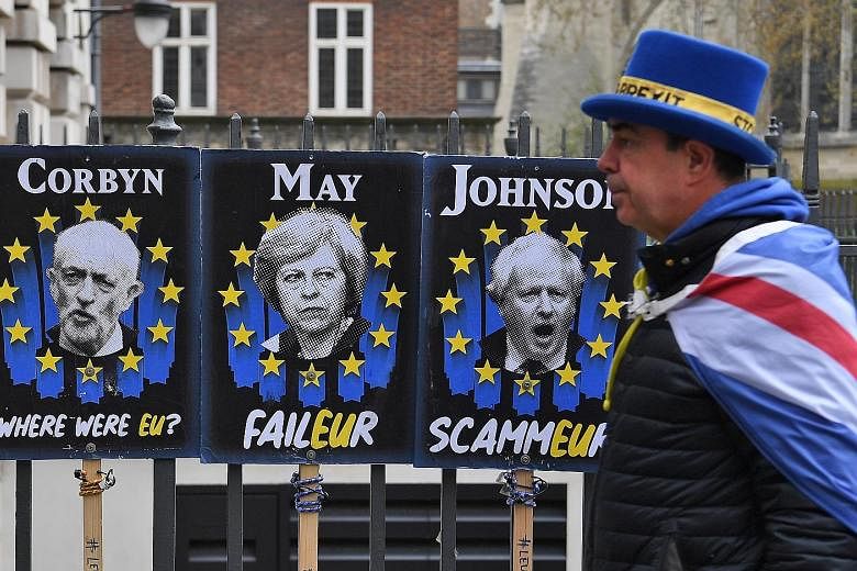 A pro-EU campaigner walking past posters mocking British politicians Jeremy Corbyn, Theresa May and Boris Johnson in London yesterday. A group of lawmakers will try and pass a law today that will force Prime Minister May to further delay Brexit. Barr