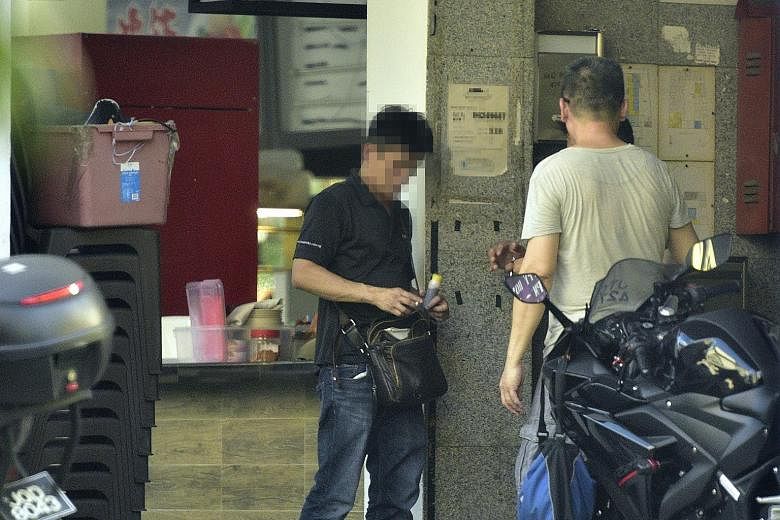 A buyer (in black) procuring a bottle of cough syrup behind a coffee shop in Geylang Lorong 7 while a minder (in grey) looks on. The bottles are hidden inside mailboxes and motorcycle top cases just a few metres away, and are retrieved once a sale is