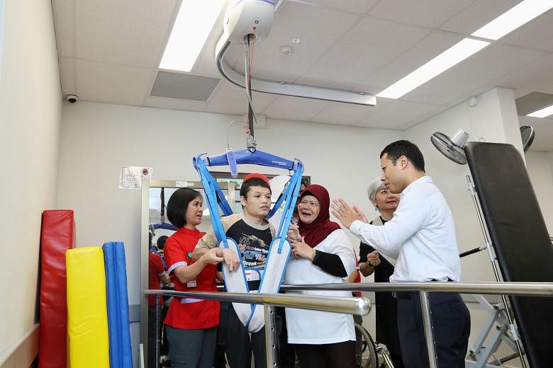 Mr Ahmad Fahmi Yusuf trying out a mechanical hoist in the new Day Activity Centre in Jurong West as Mr Desmond Lee, Minister for Social and Family Development, looks on.