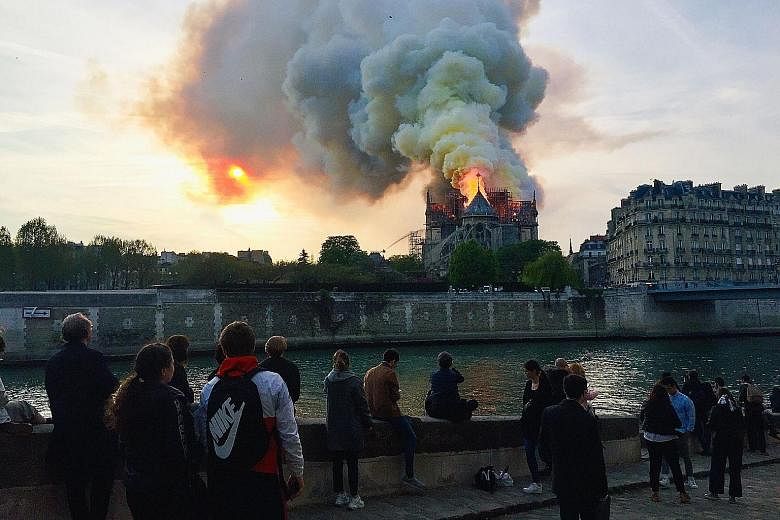 People watching in shock as smoke billowed from the top of the famed Notre-Dame Cathedral on Monday. French media reported that the fire may be linked to renovation work on the roof and the spire. PHOTO: AGENCE FRANCE-PRESSE Above: A woman overwhelme