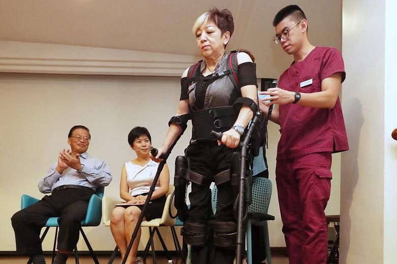 Ms Teresa Tan walking on stage with the aid of an exoskeleton suit and a hospital staff member at the launch of the Temasek Foundation - Improving Mobility via Exoskeletons (iMOVE) programme at Alexandra Hospital yesterday. With them are fellow iMOVE