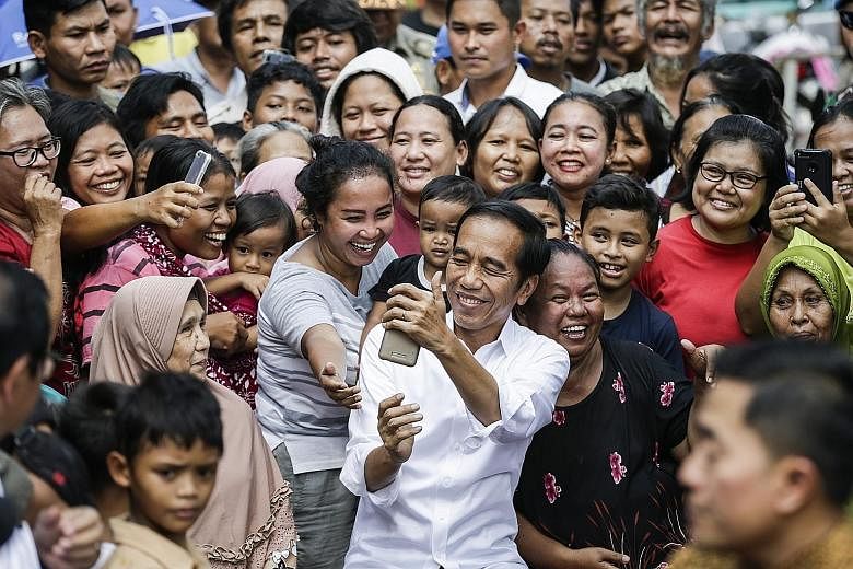 President Joko Widodo taking photographs with residents of a slum area in Jakarta following his victory speech yesterday, in which he pledged to be a leader and protector of all Indonesians.