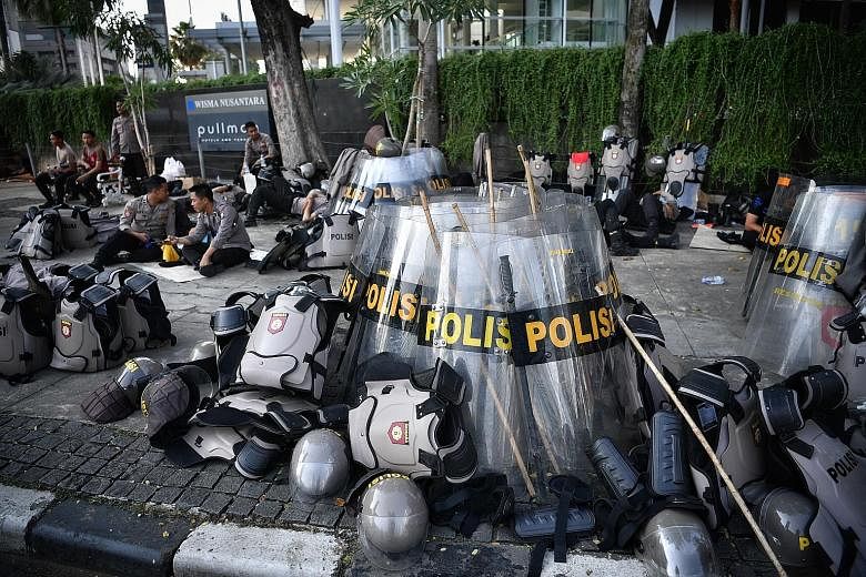 Right: Workers cleaning up debris yesterday after the previous night's violent clashes between police and rioters in Jakarta. Above: Police officers taking a breather. ST PHOTOS: ARIFFIN JAMAR