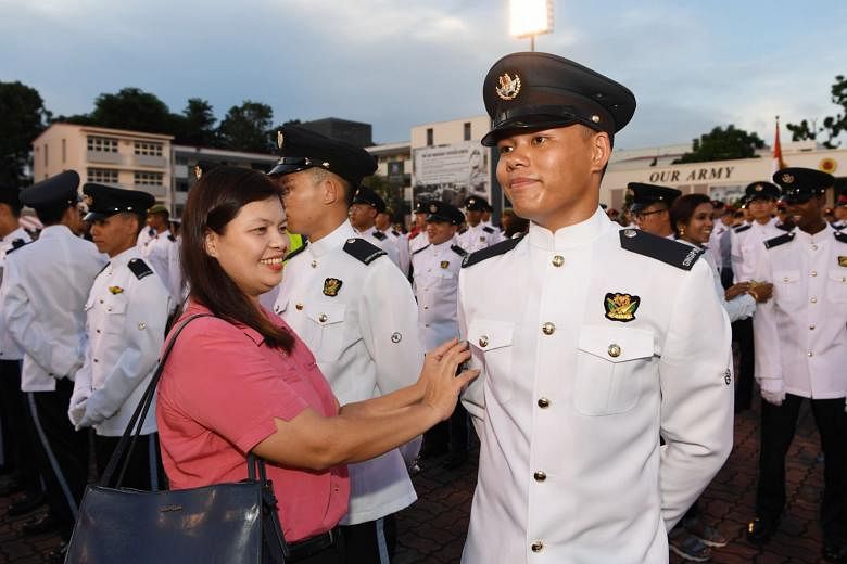 Third Sergeant Dela Cruz Carl Stephen Linao's mother affixing his rank to his uniform at the parade at Pasir Laba Camp. He was among the 1,000 cadets who graduated as full-fledged specialists yesterday.