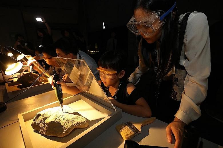 Visitors drilling into rocks to uncover fossils in a hands-on activity at the DinoQuest exhibition in Science Centre Singapore yesterday. The exhibition, which uses digital technology such as holograms, will be open to the public from next Saturday t