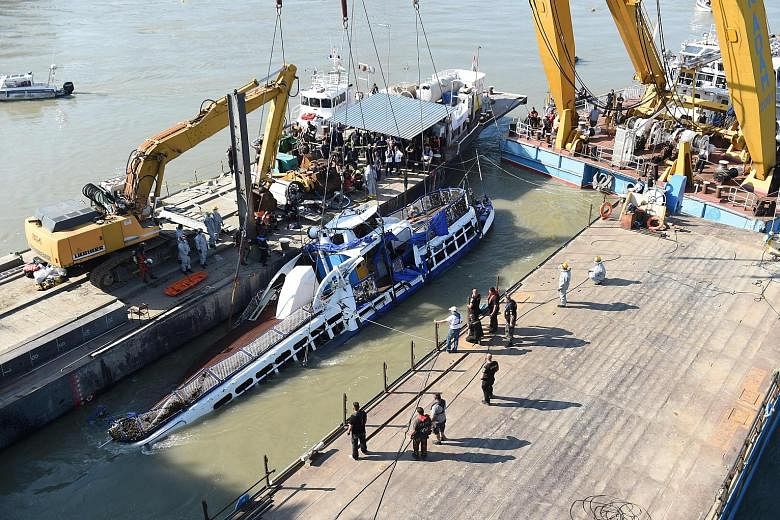 Right: Workers using a giant crane to lift the Mermaid from the Danube in Budapest yesterday. The tourist boat capsized in an accident on May 29. Above: Salvage workers saluting in respect before one of the four bodies recovered yesterday. PHOTOS: AG