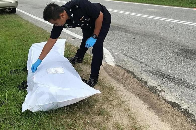 A policeman attending to the body of Mr Xavier Liaw Xiang E, 42, who was killed yesterday when he was thrown from his BMW motorcycle at a road junction in Gelang Patah, Johor, about 15km from the Tuas Second Link. PHOTO: ISKANDAR PUTERI POLICE