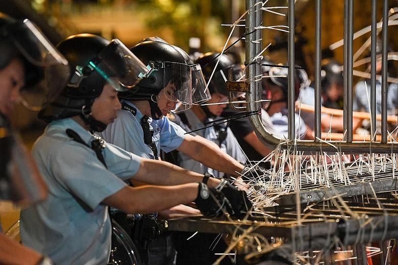 Officers clearing the barricades outside the police headquarters early yesterday morning. The protesters had set up the barricades secured with cable ties to cut off access to the complex. Some security and police personnel cleaning and covering up t