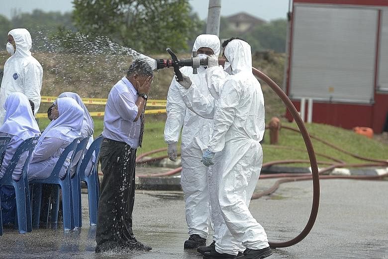 Health officials carrying out decontamination work yesterday at Johor's Pasir Gudang Indoor Stadium, where an early treatment centre was set up for dozens of students suffering from vomiting and breathing difficulties after attending schools nearby.