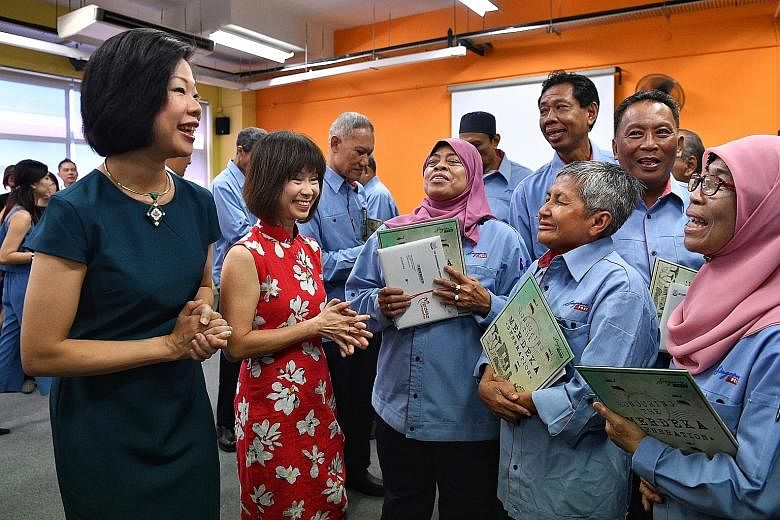 Senior Minister of State for Communications and Information Sim Ann (left) and Senior Minister of State for Health Amy Khor chatting with postal workers from the Merdeka Generation at the SingPost Kallang Delivery Base yesterday after they received t