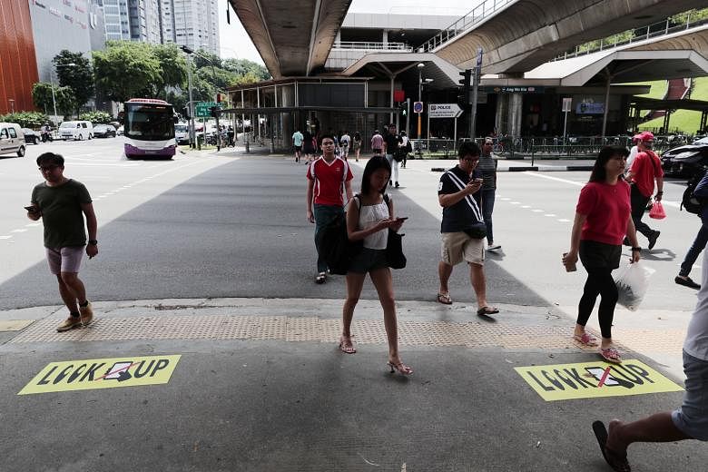Despite stickers and small billboards reminding pedestrians not to be distracted while crossing the road near Ang Mo Kio MRT station, many were seen glued to their devices yesterday. ST PHOTO: KELVIN CHNG