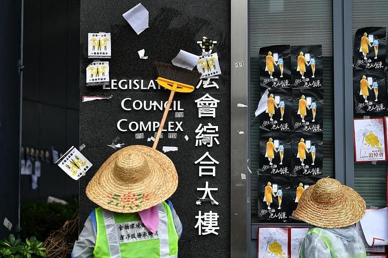 Cleaners scraping off posters put up by protesters at the Legislative Council Complex in Hong Kong yesterday as the city cleaned up after the overnight violence. Calm returned to the city yesterday, but the LegCo building was sealed off by police. Al