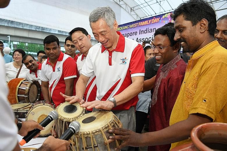 Prime Minister Lee Hsien Loong trying out the tabla, a traditional Indian percussion instrument, yesterday at the Sengkang West Family Day, as Senior Minister of State for Health and Transport, and MP for Sengkang West, Dr Lam Pin Min, looks on. With