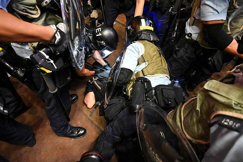 Above: A woman confronting a police officer with a poster critical of the police's handling of protesters. ST PHOTO: CHONG JUN LIANG Right: Police officers arresting a protester after a separate group of marchers took to the streets in Mongkok last n