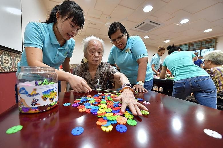 Madam How Lin Chi playing a game with guidance from her live-in caregiver Lai Lai Win (far left) and Ms Massuriyantee Othman (left), a healthcare assistant at Ghim Moh Senior Care Centre.