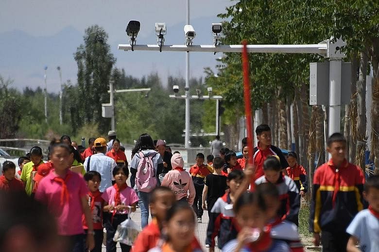 Schoolchildren walking below surveillance cameras in Akto, in China's western Xinjiang region. In China, surveillance is becoming pervasive, and algorithms score citizens on their behaviour. The writer says it has been argued that if the West enacts 