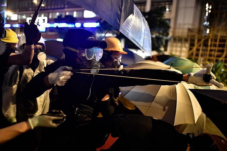 A protester using a slingshot to fire projectiles at police. Some hurled objects like bottles, rocks and umbrellas at officers, or pushed flaming objects - including rubbish bins and a metal cart - at them. PHOTO: AGENCE FRANCE-PRESSE Protesters runn