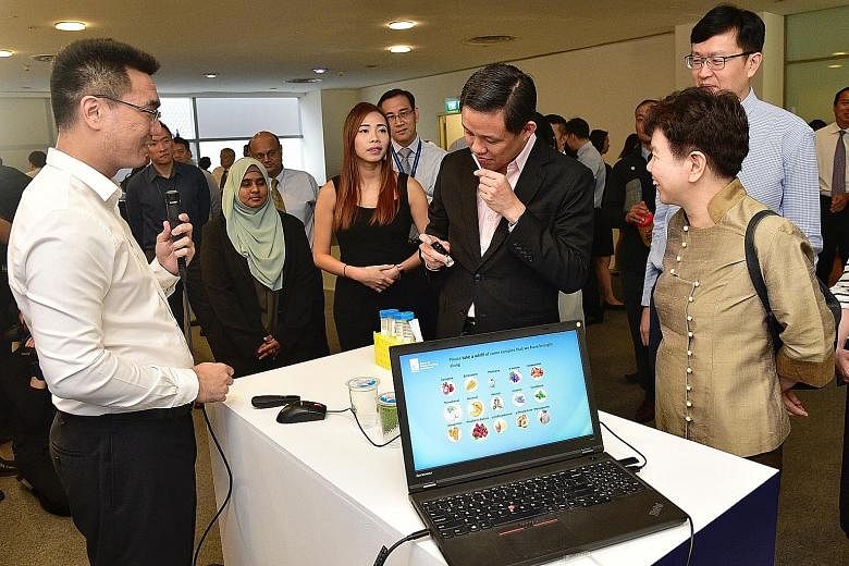 Research fellow and former A*Star scholarship recipient Andy Ng Yao Zong (left) watching as Trade and Industry Minister Chan Chun Sing takes a whiff of a fragrance produced by bio-engineered yeast cells. With them are (from right) A*Star chairman Cha