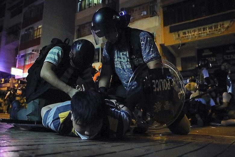 Above: Lawyers on their silent march in Hong Kong yesterday. Left: A protester being arrested in Sham Shui Po district, where a group of demonstrators laid siege to a police station on Tuesday after the arrest of a student leader. PHOTOS: ASSOCIATED 