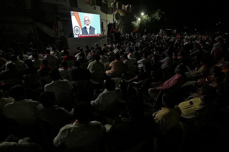 People watching a broadcast of Prime Minister Narendra Modi delivering his televised address to the nation in Ahmedabad, India, yesterday. The decision to withdraw Jammu and Kashmir's special status and bifurcate the state has had domestic and intern