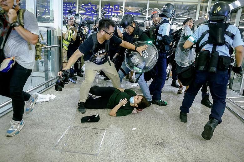 Above: A tourist passing her luggage to security guards as she tried to enter a departure gate yesterday amid another demonstration by anti-government protesters at Hong Kong International Airport. PHOTO: AGENCE FRANCE-PRESSE Right: Riot police tryin