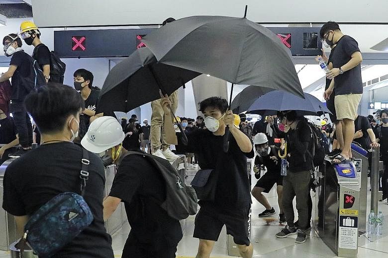Demonstrators using umbrellas to evade closed-circuit television cameras during a protest at the Yuen Long metro station on Wednesday night to mark the July 21 attack there on pro-democracy protesters and other commuters by a mob of white-clad men ar