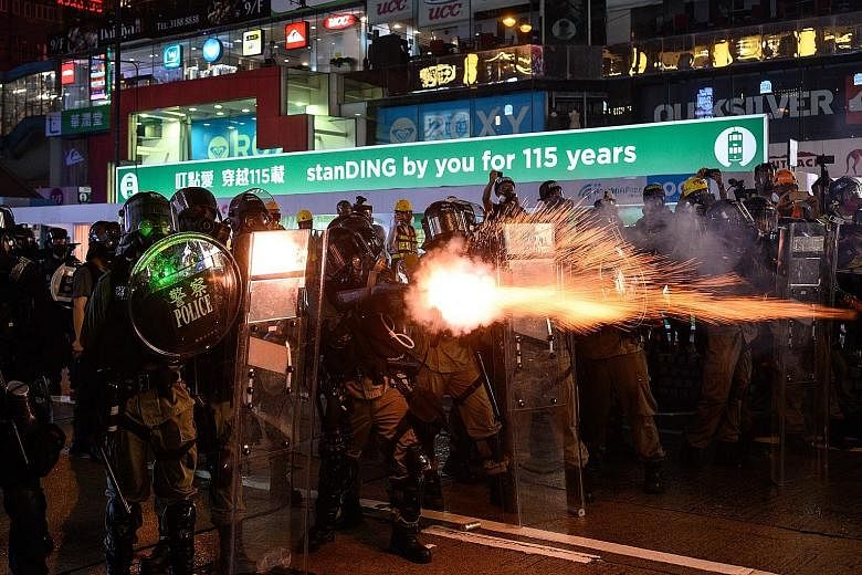 A protester hurling back an exploded tear gas shell, as the police shot blue-coloured water from water cannon in central Hong Kong yesterday. Thousands of demonstrators marched in the muggy weather armed with umbrellas.