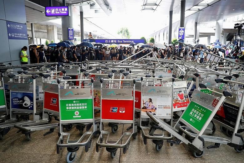 Far left: An airline crew member trying to make his way through a makeshift barricade made by protesters using luggage trolleys at Hong Kong International Airport yesterday. Left: The makeshift barricade. PHOTO: REUTERS An anti-government protester t