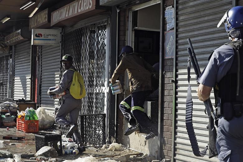 Looters making off with goods from a store as a riot police officer approached in Germiston, east of Johannesburg, South Africa, yesterday. Hundreds marched through the streets on Monday in an unusually large display of anti-foreigner sentiment. More