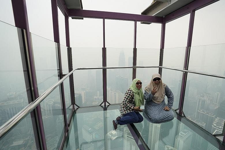 Tourists posing for a picture at the Skybox in the Kuala Lumpur Tower yesterday as the cityscape was shrouded in haze. The Selangor state government has decided to conduct cloud seeding in areas where the Air Pollutant Index reading exceeds the very 