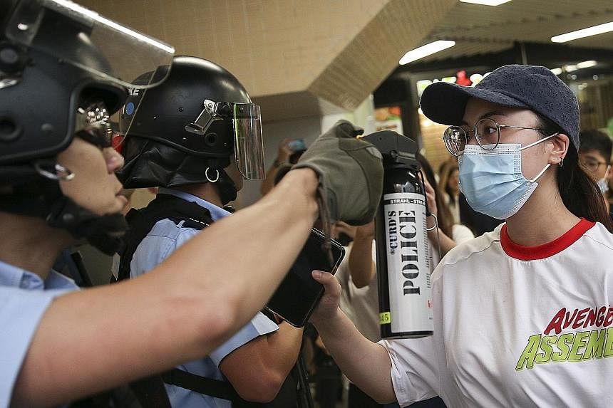 A police officer aiming pepper spray at a demonstrator as anti-government protesters and pro-China supporters scuffled inside a shopping mall in Hong Kong yesterday. Pro-China supporters fighting with anti-government protesters in the Kowloon Bay dis