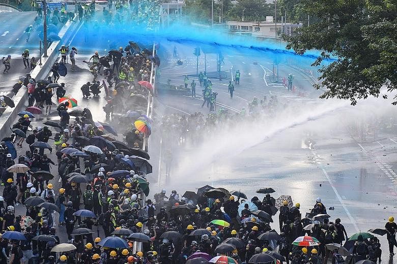 Police using water cannon outside the government headquarters in Hong Kong to disperse protesters yesterday. One water cannon was spraying blue jets of water, which make protesters easier to identify later. A protester on fire after throwing a Moloto