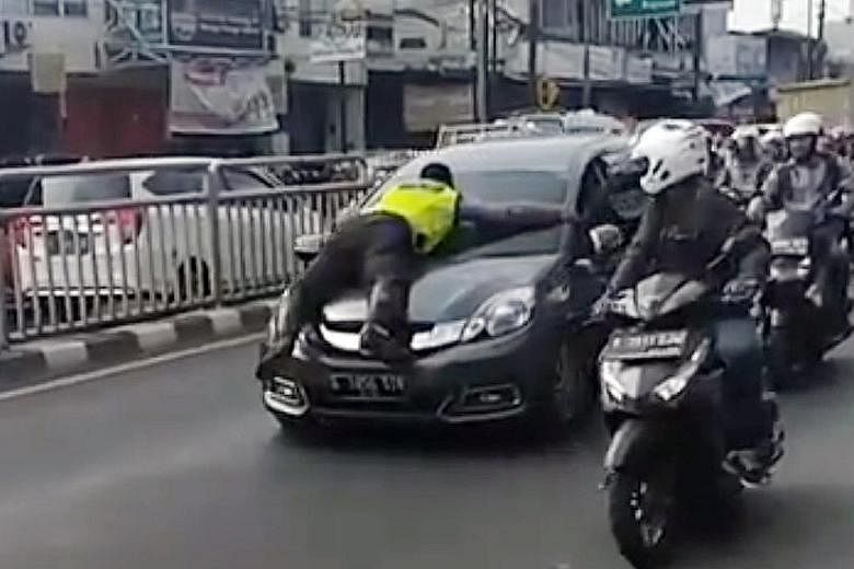 A screengrab of an online video showing a police officer in Jakarta trying to stop a driver from fleeing to avoid a parking ticket. PHOTO: JKTINFO/INSTAGRAM