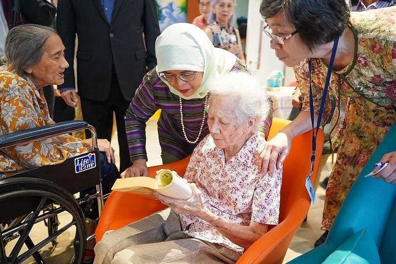 President Halimah Yacob checking out a book on dementia held up by Madam Mary Sng, a 92-year-old resident of Apex Harmony Lodge in Pasir Ris. Madam Halimah yesterday toured the premises of the long-term residential care facility for people with demen