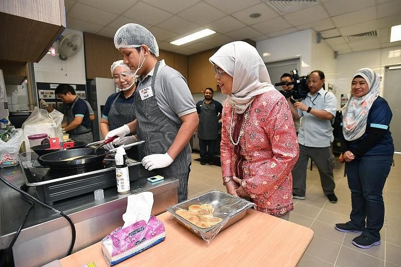 President Halimah Yacob watching Hadi Ukasyah Noor Asahar, 14, prepare food in the kitchen of Colours Cafe at St Andrew's Autism School yesterday. The in-house school cafe is run by students capable of work, so that they can develop skills and work h
