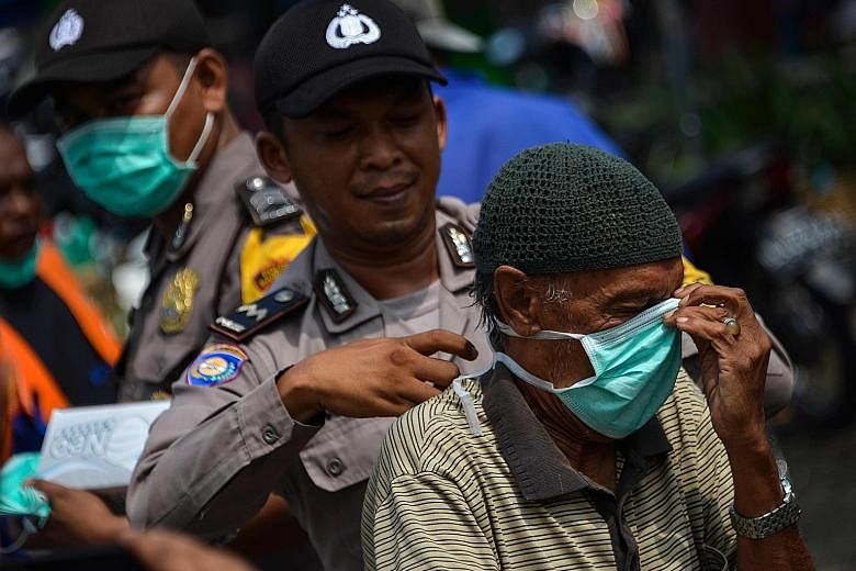A police officer helping a motorist put on a face mask in Banda Aceh, in Sumatra, yesterday. There were 3,150 hot spots across Indonesia on Monday. But by Tuesday, the number had dropped sharply to 1,982 before slipping to 1,744 yesterday, Indonesia'