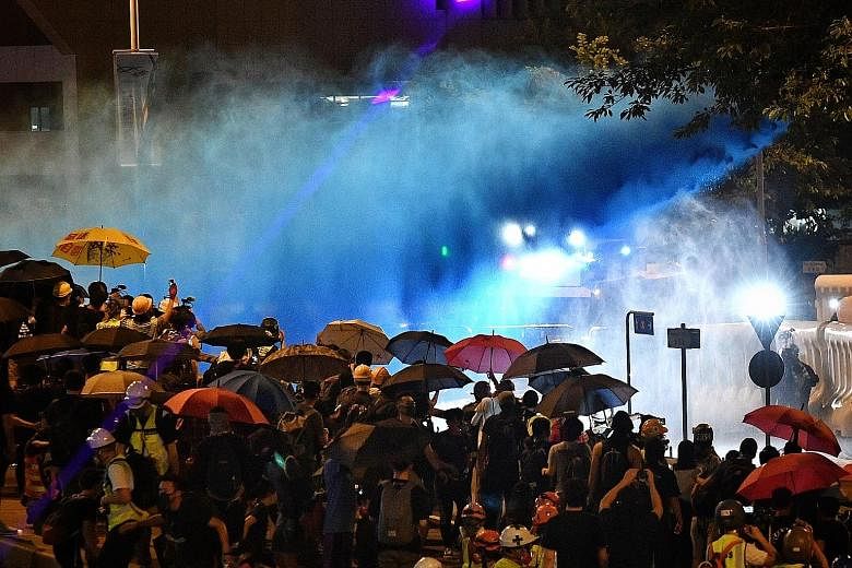 Police spraying blue dye from a water cannon truck at the sea of umbrella-shielded protesters yesterday. Protesters put up barricades in Harcourt Road, which was also carpeted with pro-democracy posters.
