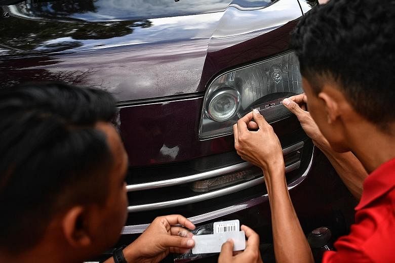 A radio frequency identification tag for Malaysia's Vehicle Entry Permit scheme being placed on the headlamp of a car in Johor Baru in July. The scheme is meant to cover foreign-registered cars entering Malaysia from Singapore.