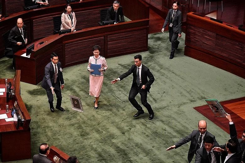 Security aides rushing to shield Hong Kong Chief Executive Carrie Lam after a pro-democracy legislator threw a placard at her while she was leaving the Legislative Council yesterday. Pro-democracy lawmakers disrupted Mrs Lam's annual policy address, 