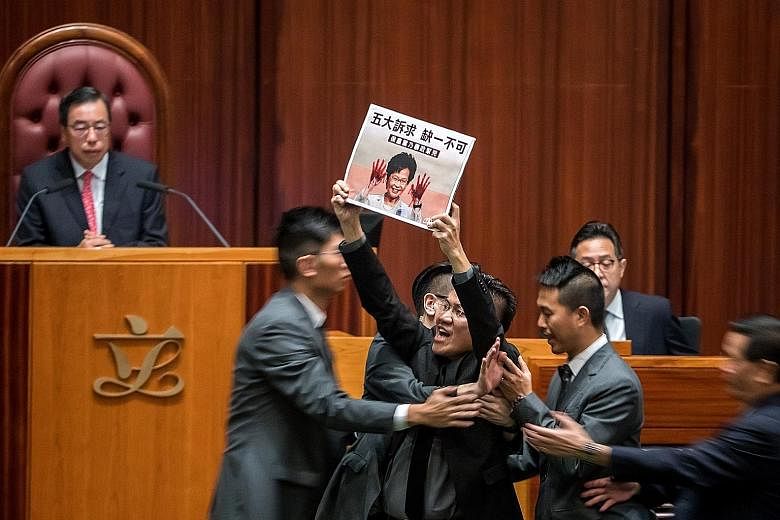 Above: Chief Executive Carrie Lam arriving for a question-and-answer session at the Legislative Council in Hong Kong yesterday amid noisy protests from pro-democracy lawmakers. Right: Lawmaker Gary Fan protesting during the Legislative Council sessio
