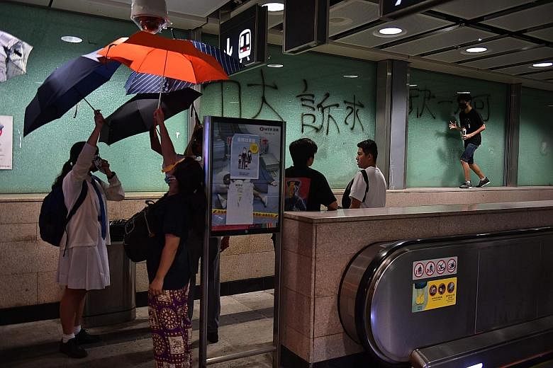 Protesters obscuring a security camera with umbrellas as another spray-painted graffiti at an MTR station yesterday.