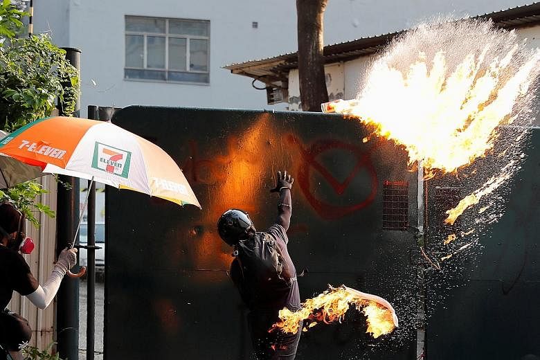 A protester throwing a petrol bomb at Tsim Sha Tsui Police Station during a rally on Sunday. Hong Kong has been riven by seething protests for the past 20 weeks, with violence spiralling on both sides of the ideological divide. PHOTO: REUTERS